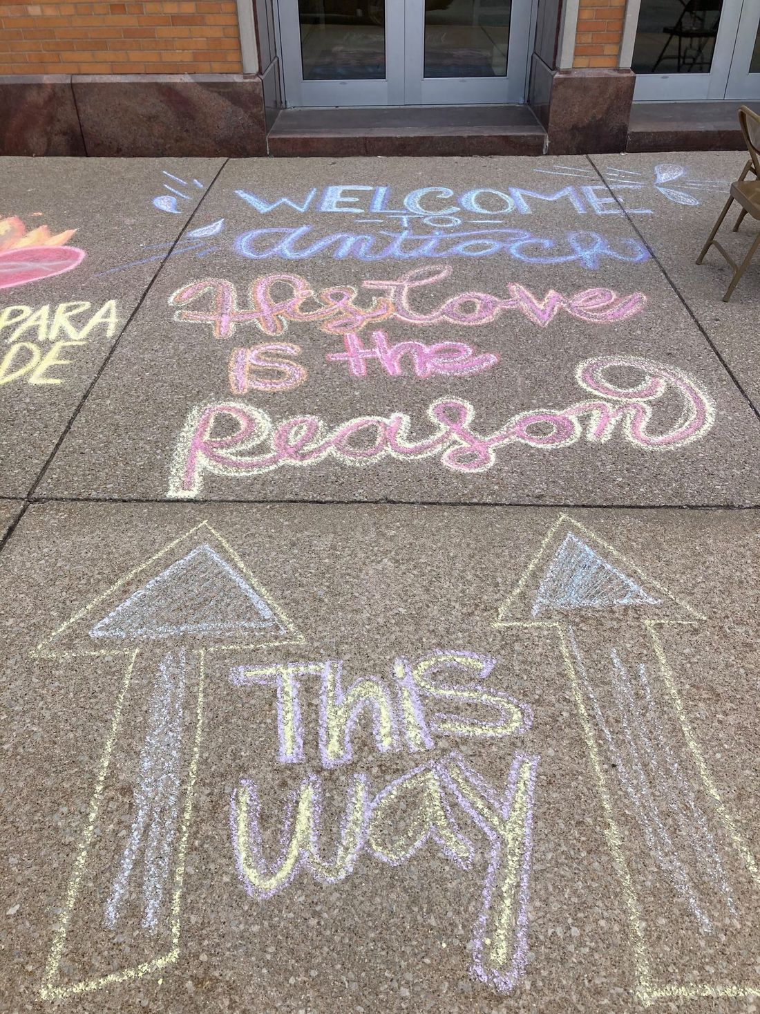 Sidewalk chalk outside the parish reading Welcome to Antioch, Love is the Reason, with arrows pointing the way in